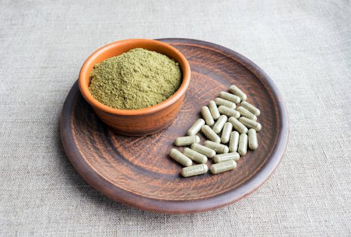 An arrangement of fresh kratom capsules, and kratom powder, representing the different forms of kratom available to users.